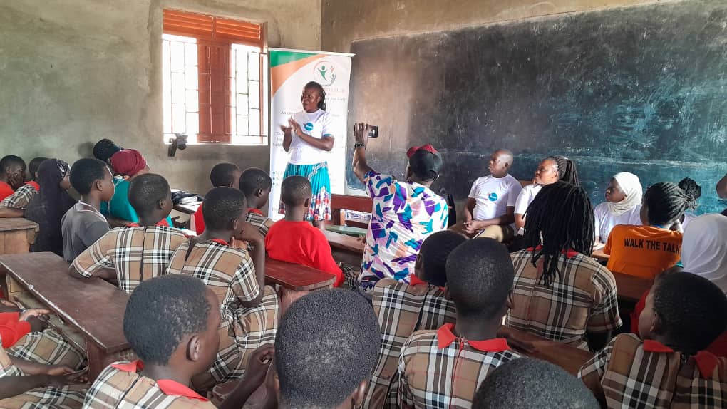 A classroom scene with a female educator speaking to a group of students, who appear engaged. The students are wearing school uniforms, while the educator is in a white shirt. A FlowReady banner is visible in the background.